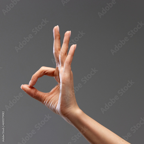 Female hand showing gesture of OK against grey background. Good time, approvement signals, acceptance. Concept of human relation, community, symbolism, culture, cummunication photo