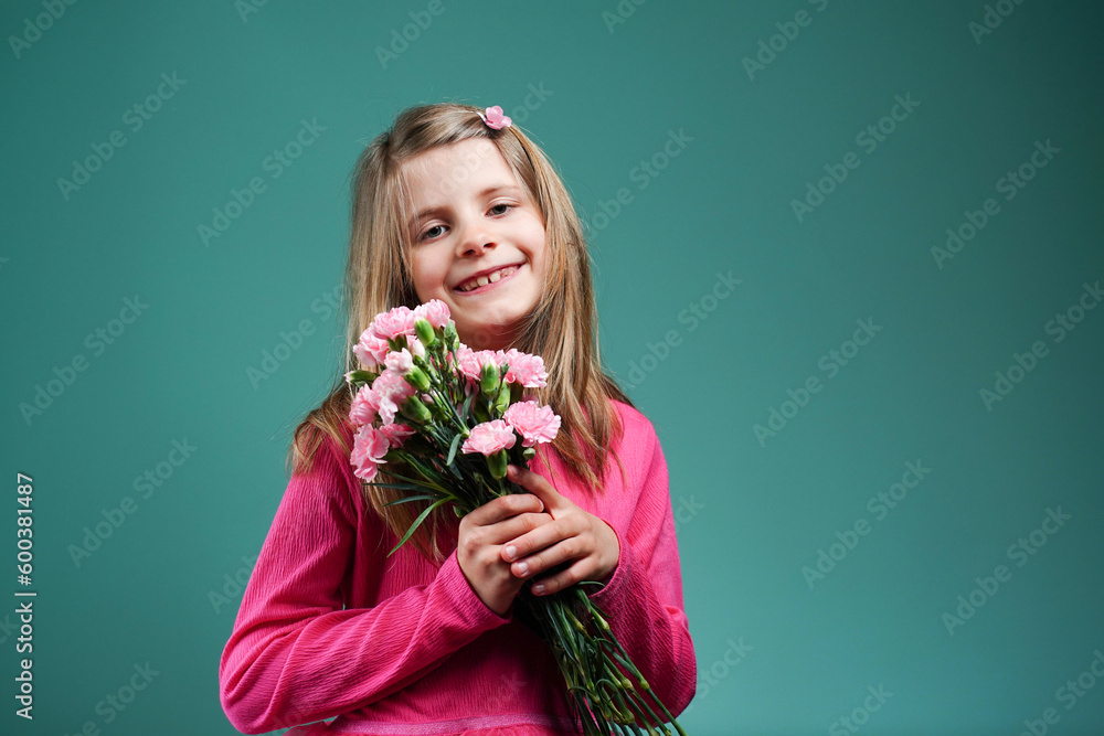 Happy smiling girl in a pink dress holding a bouquet of pink carnations on a blue green turquoise background. Congratulations. Concept for Mother's Day. Copy space Happy smiling girl in a pink dress holding a bouquet of pink carnations on a blue green turquoise background. Congratulations. Concept for Mother's Day. Copy space
