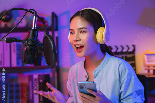 Cheerful beautiful Asian woman wearing headphones and using laptop record podcast at night. Content creator concept. photo