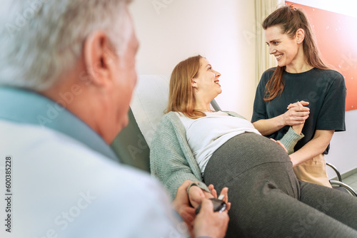 Lesbian Couple with Gynecologist during Pregnancy Checkup - Senior gynecologist checks blood sugar of a happy pregnant lesbian woman, her partner touches her belly.