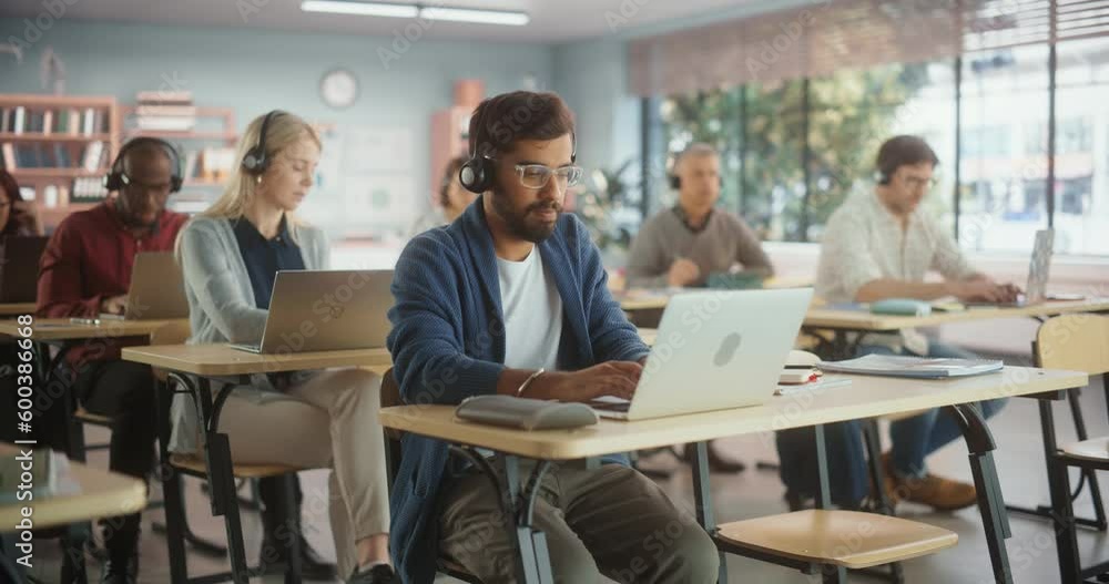 Diverse Mature Students Learning in Classroom, Sitting Behind Desks with Headphones, Using Laptops and Writing in Notebooks. Teacher Giving an Adult Education Course Remotely Online Diverse Mature Students Learning in Classroom, Sitting Behind Desks with Headphones, Using Laptops and Writing in Notebooks. Teacher Giving an Adult Education Course Remotely Online