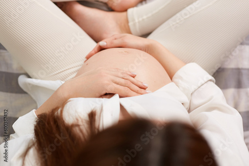 Pregnancy, love, healthcare, motherhood, people, relaxation and expectation. Young beautiful pregnant woman sitting holding her belly in top view.