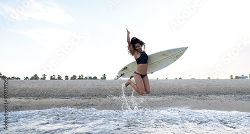 Happy woman jumping with surfboard