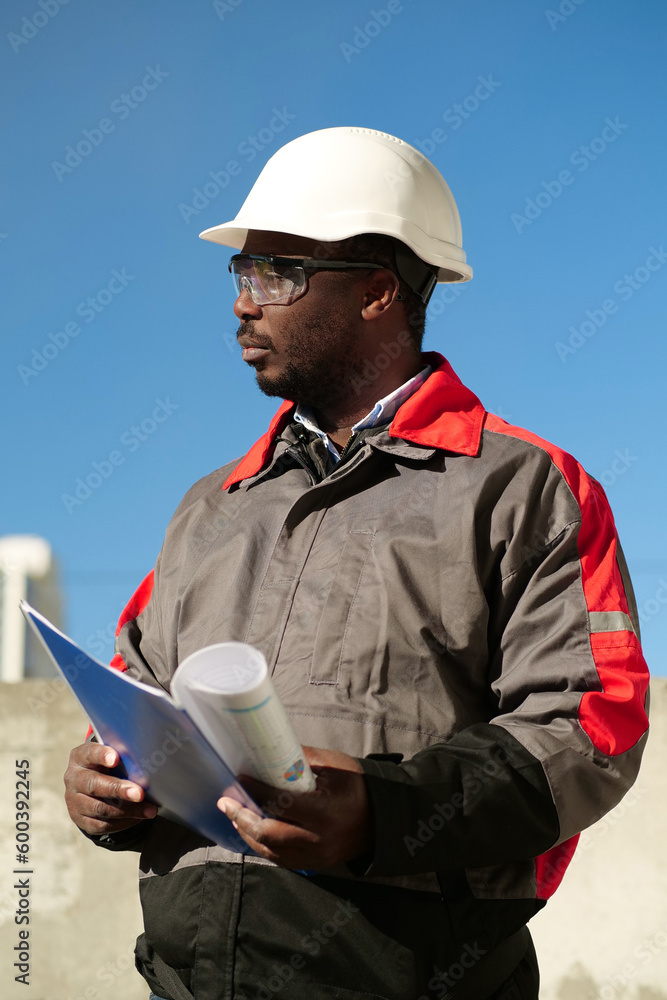 African american worker stands at construction site with work papers African american worker stands at construction site with work papers