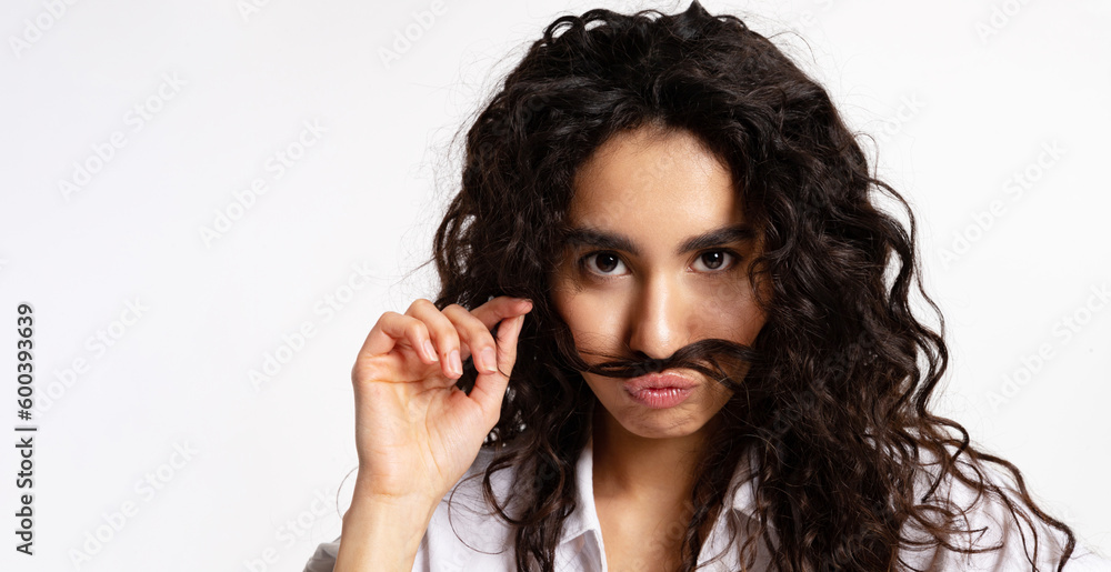 A beautiful girl fools around and makes a mustache out of a strand of her hair and looks at the camera