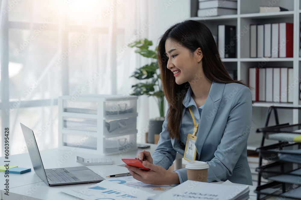 Happy business woman using mobile phone while working at office with laptop. Smiling business woman messaging with smartphone. Beautiful stylish business woman browsing site on cellphone Happy business woman using mobile phone while working at office with laptop. Smiling business woman messaging with smartphone. Beautiful stylish business woman browsing site on cellphone