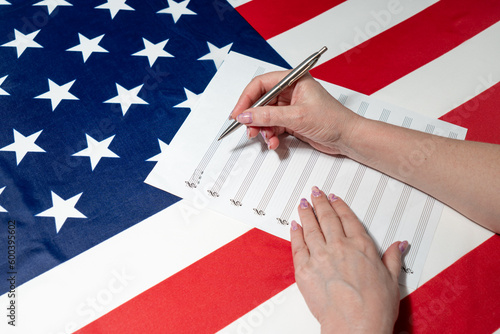 Close-up of female hands writing musical notes on a sheet of sheet music, against the background of the American flag photo