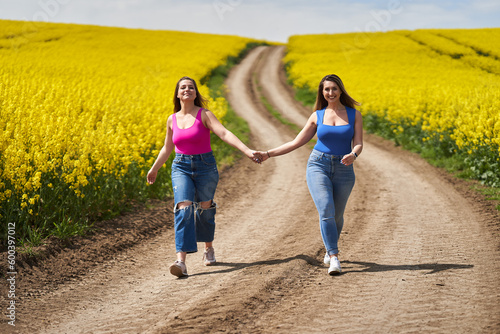 Plus size women walking on a road through canola fields together holding hands © Xalanx