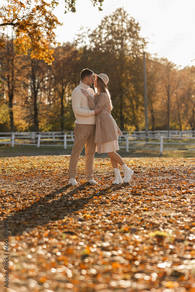 Fototapeta premium Young stylish couple lovers are hugging and kissing in the autumn park. Lovely romantic moment between man and woman in love, looking to each others. Happy family. Love, youth, happiness concept.