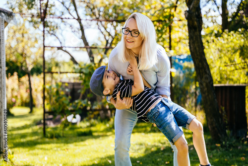 Young blond woman playing with her son on nature in the garden at summer sunny day. Freedom, love, childhood, relation concept.