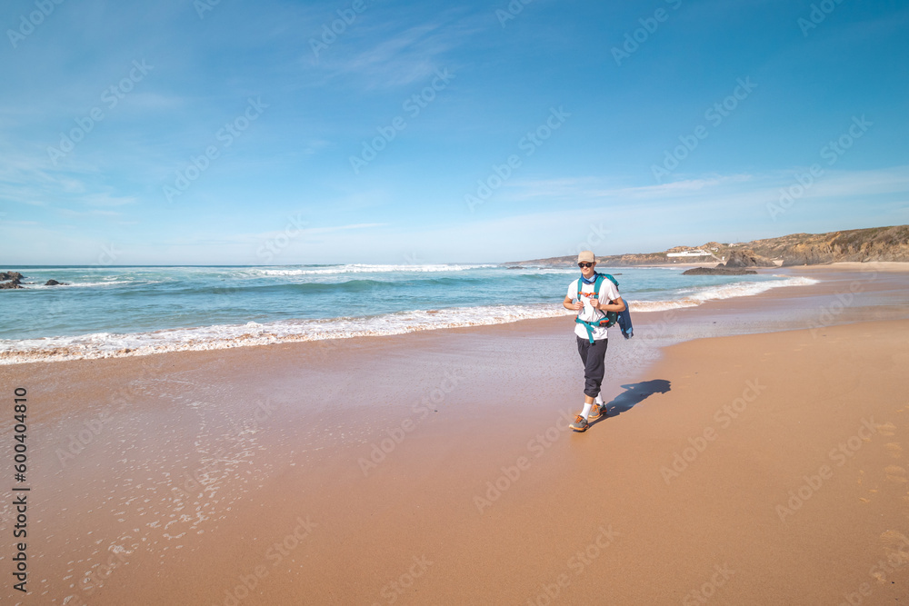 Backpacker walks along Praia do Almograve with a smile on his face. The joy of moving and discovering new places. Odemira region, western Portugal. Wandering along the Fisherman Trail, Rota Vicentina Backpacker walks along Praia do Almograve with a smile on his face. The joy of moving and discovering new places. Odemira region, western Portugal. Wandering along the Fisherman Trail, Rota Vicentina