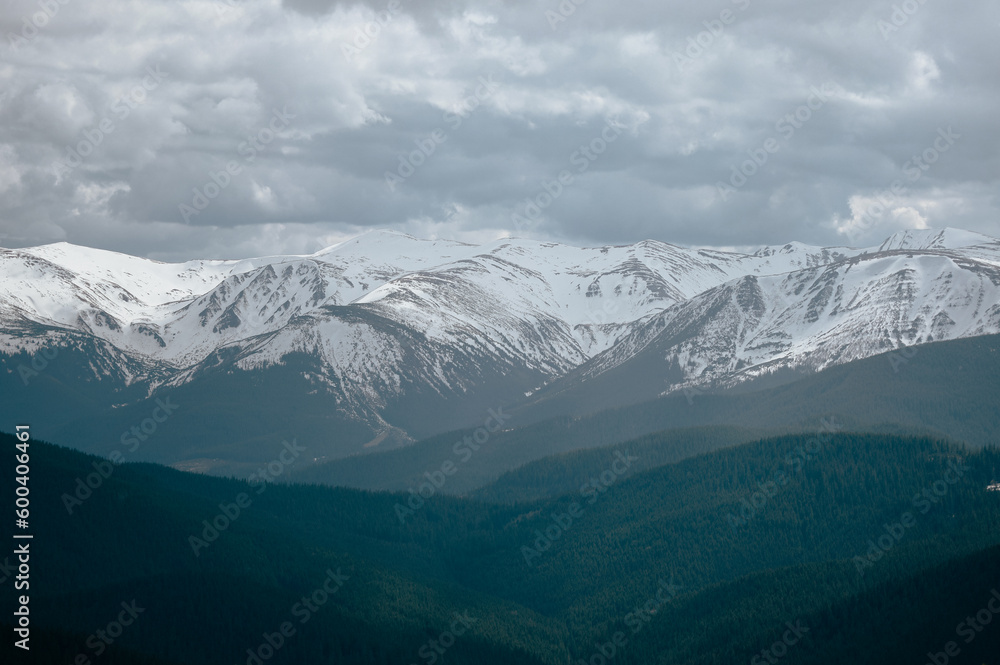 snowy mountains with a forested valley and a cloudy sky