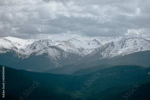 snowy mountains with a forested valley and a cloudy sky
