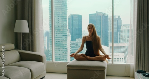 Tableau sur toile Woman meditating breathing by the window with view on modern buildings skyscrapers of a big city