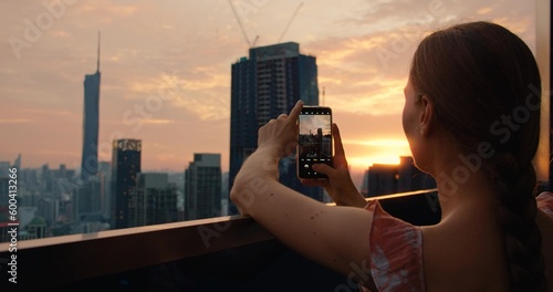 Canvas Print Woman on roof of skyscraper shoots a city landscape on a mobile phone during sunset