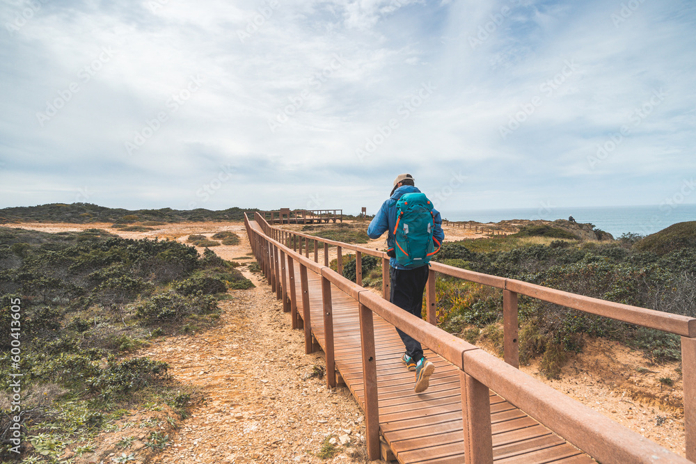 Young and courageous Vagabund roaming the Portuguese countryside. A backpacker walks along a wooden walkway in the Odemira region of Portugal. Fisherman Trail, Rota Vicentina