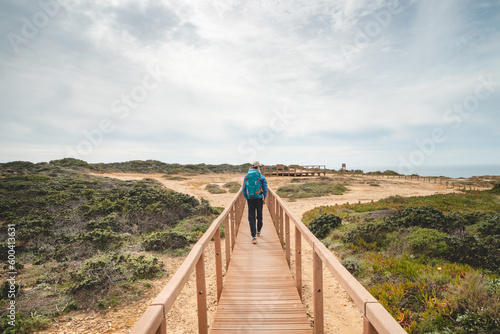 Young and courageous Vagabund roaming the Portuguese countryside. A backpacker walks along a wooden walkway in the Odemira region of Portugal. Fisherman Trail, Rota Vicentina photo