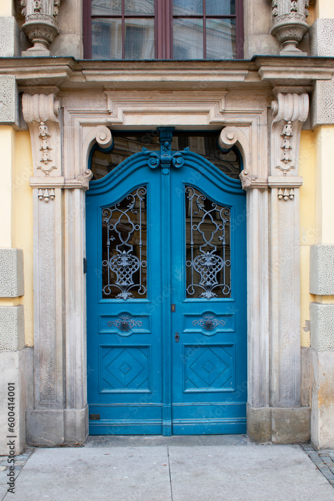 View of an old blue door with decorative elements on the facade of an antique building with beige and yellow walls, columns and sculptures. Poland, Wroclaw, January 2023.