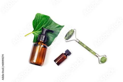 Brown cosmetic bottles, green leaf and jade face roller on white background. Top view, flat lay