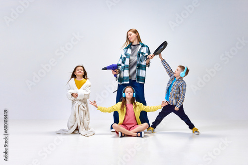 Domestic lifestyle. Portrait of young woman, other and little kids, children posing in home wear against grey studio background. Concept of family, motherhood, childhood, fashion, lifestyle