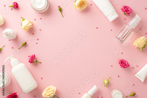 Soft and gentle natural skincare with a top view flat lay of exquisite cream bottles, pump bottles, and pipettes with delicate rose flowers on pastel pink background. The empty space is for text