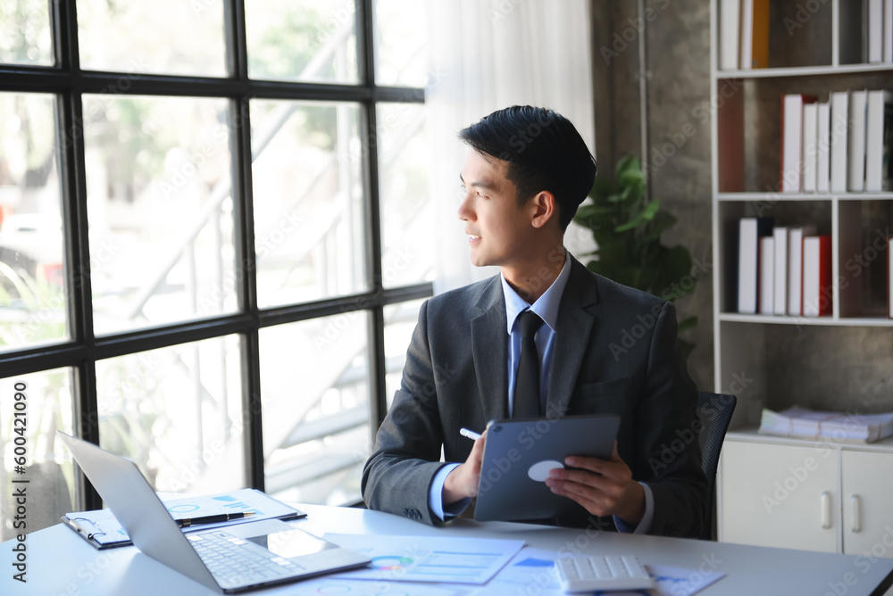Young business man working at office with laptop, tablet and taking notes on the paper..