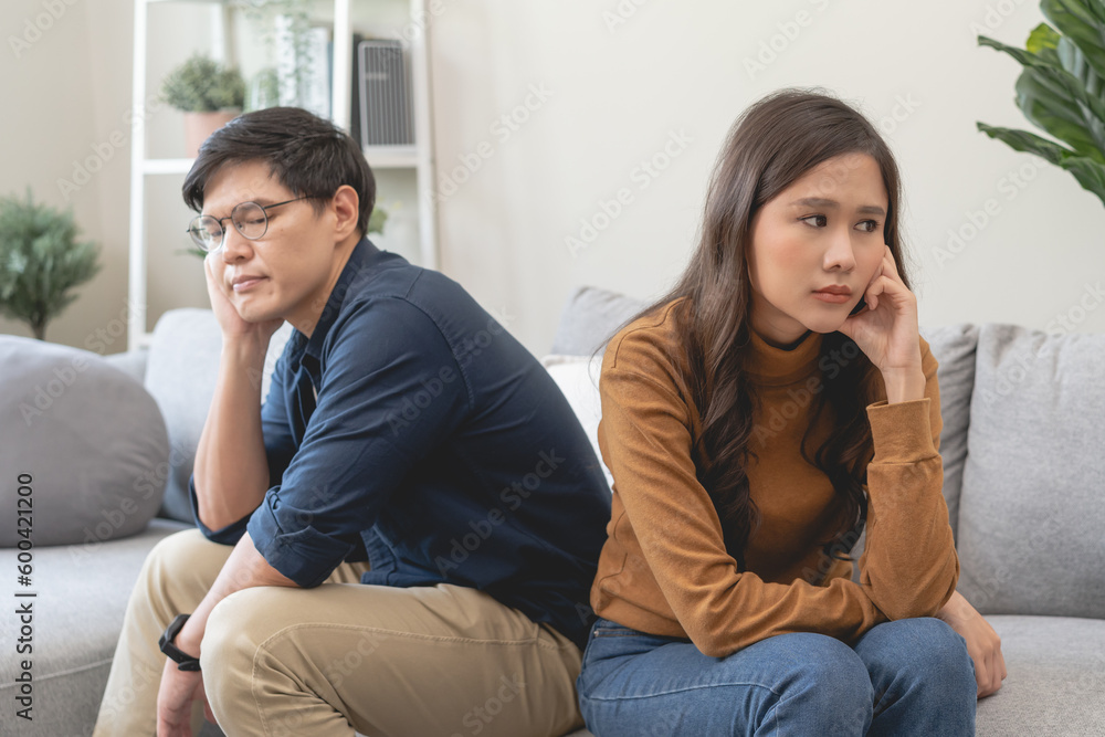 Family problem concept, Asian wife and husband sitting back to back in the living room at home have problems in a relationship and have an argument Family problem concept, Asian wife and husband sitting back to back in the living room at home have problems in a relationship and have an argument