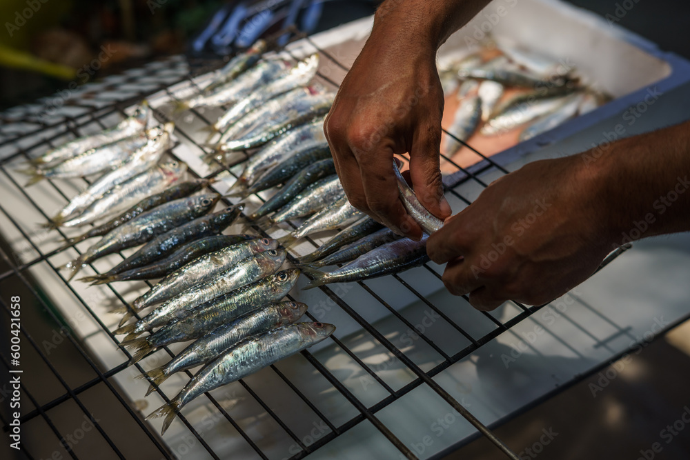 Hands placing fresh sardines on the grill. - obrazy, fototapety, plakaty 
