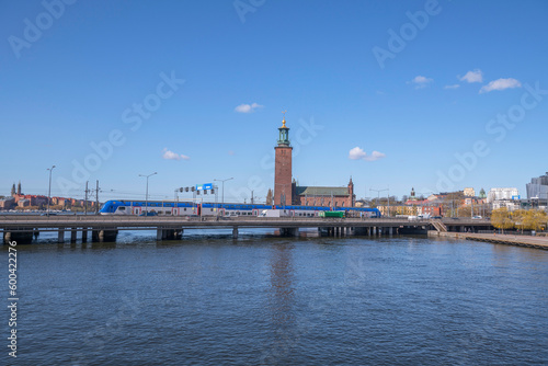 Blue commuter train on a bridge over the river Strömmen in front of the Town City Hall, a sunny spring day in Stockholm