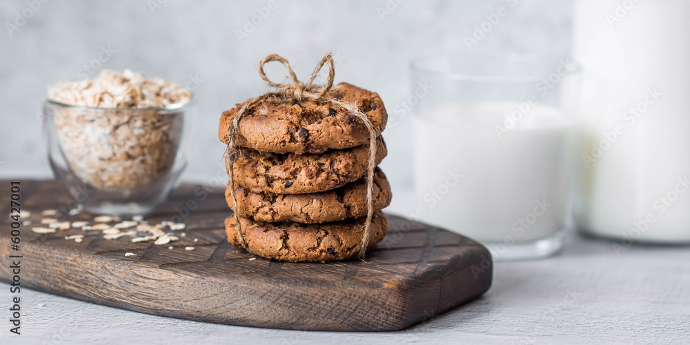 Fototapeta premium Organic natural cow's milk in a glass bottle, oatmeal and oatmeal cookies on a stylish wooden board on a stone table. Natural eco-friendly products.