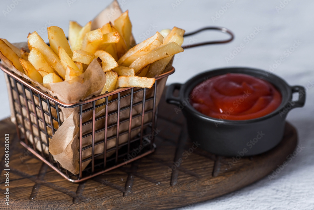 French fries in a metal basket with salt and ketchup on a stylish board on a concrete kitchen table. Fried potatoes. The concept of fast food and junk food.