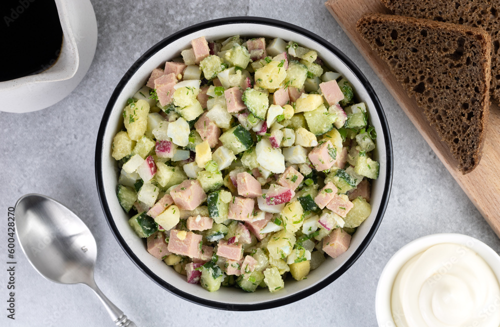 Russian cold soup - okroshka with vegetables, sausage, herbs, kvass and black bread on a gray background. Top view.