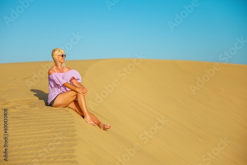 A tourist woman visiting the Maspalomas Dunes of Gran Canaria simply relaxes and sunbathes on the nearby Maspalomas Beach.