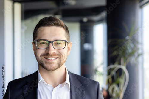 Close-up photo portrait of young successful entrepreneur, businessman investor wearing glasses at workplace smiling and looking at camera