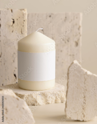 Candle with label on beige near cream travertine stones, Close up. Packaging mock up