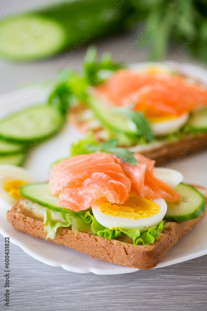 fried toast with lettuce, egg, cucumbers and red fish in a plate.