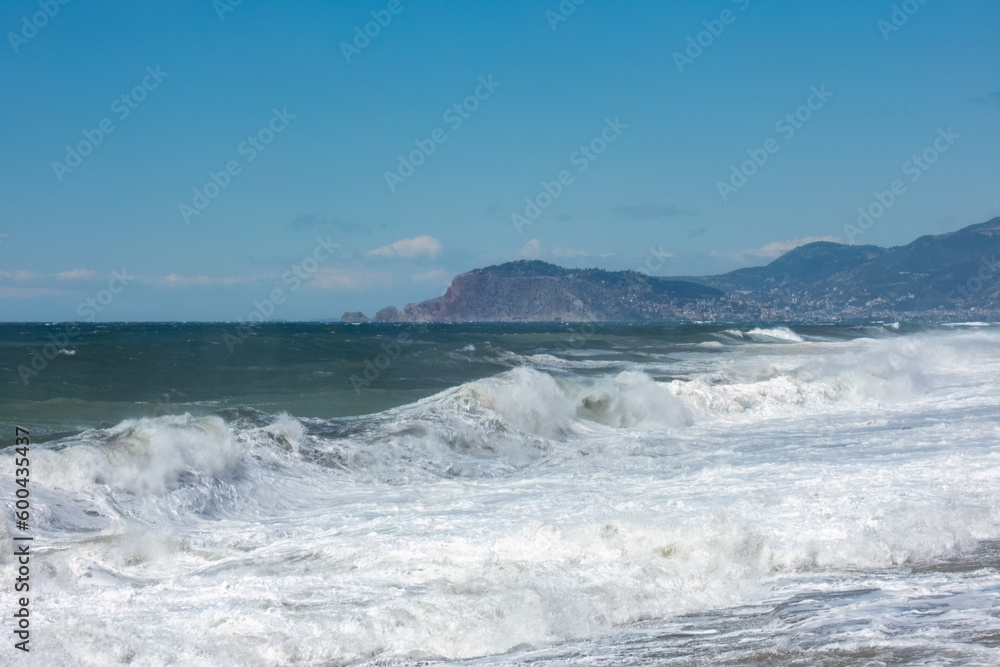 Sea waves are not far from the shore with mountains and Alanya city in the distance