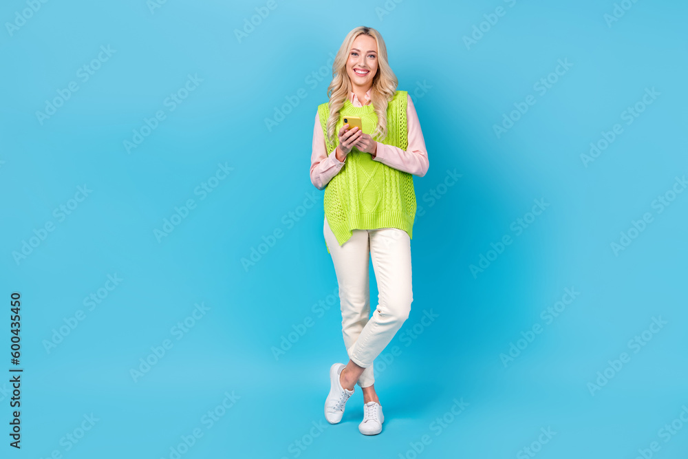 Full length photo of pretty cheerful person hold use smart phone isolated on blue color background Full length photo of pretty cheerful person hold use smart phone isolated on blue color background