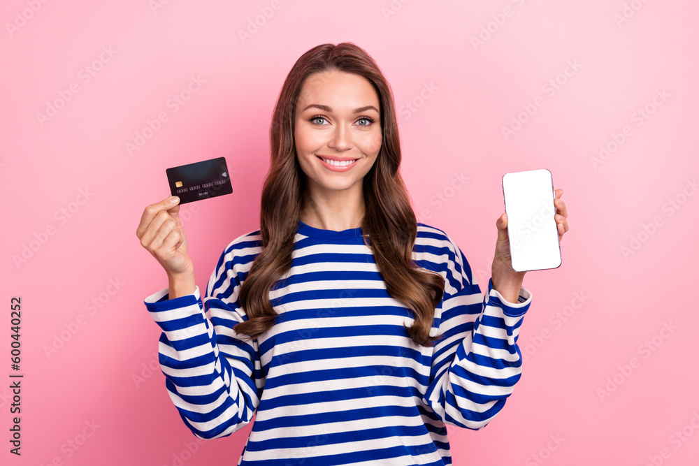 Photo portrait of satisfied young model smiling girl brown curls hold debit card smartphone display eshopping isolated on pink background Photo portrait of satisfied young model smiling girl brown curls hold debit card smartphone display eshopping isolated on pink background