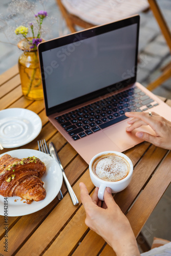 Surfing the web on a laptop in a summer cafe with a croissant and coffee
