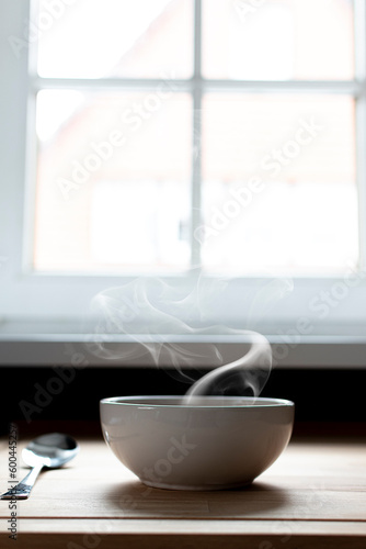 Bowl of soup next to a window. Steam of hot soup. Warm food