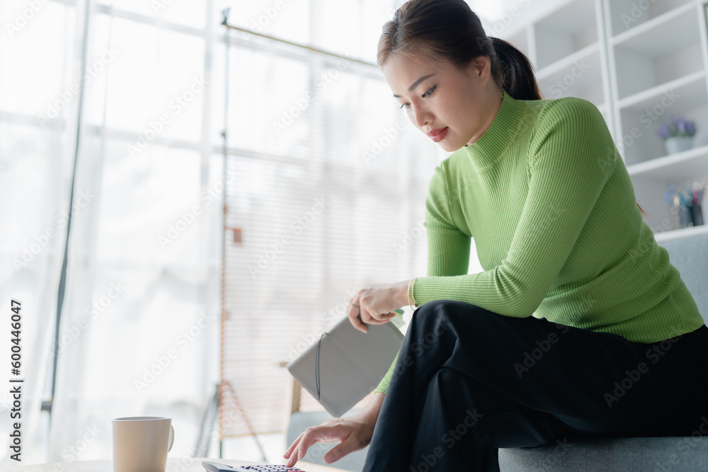 Beautiful asian women working out home finances using calculator to calculating, with invoices and paperwork on desk, living room interior. female economics accounts, cash flow expenses. Beautiful asian women working out home finances using calculator to calculating, with invoices and paperwork on desk, living room interior. female economics accounts, cash flow expenses.