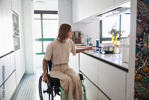 Young woman on wheelchair doing house chores in modern kitchen