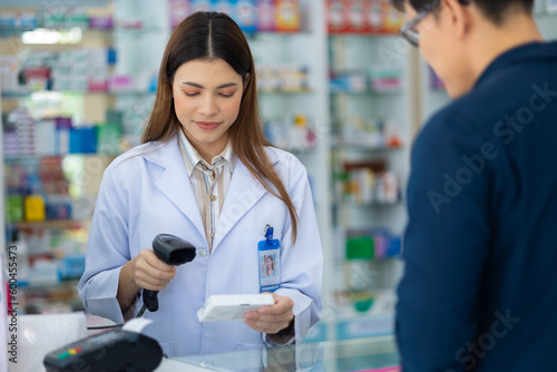 Asian female pharmacist holding bar code reader scanning pills box at the pharmacy. Shelves with drug and Health Care product