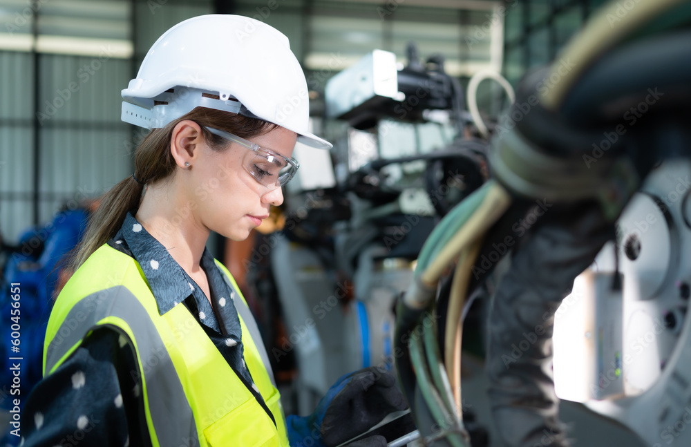 A female engineer installs a program on a robotics arm in a robot warehouse. And test the operation before sending the machine to the customer. A female engineer installs a program on a robotics arm in a robot warehouse. And test the operation before sending the machine to the customer.