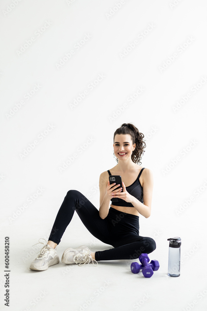 Full body fitness trainer instructor woman use mobile phone drink water train do exercises at home gym indoor. Full body fitness trainer instructor woman use mobile phone drink water train do exercises at home gym indoor.