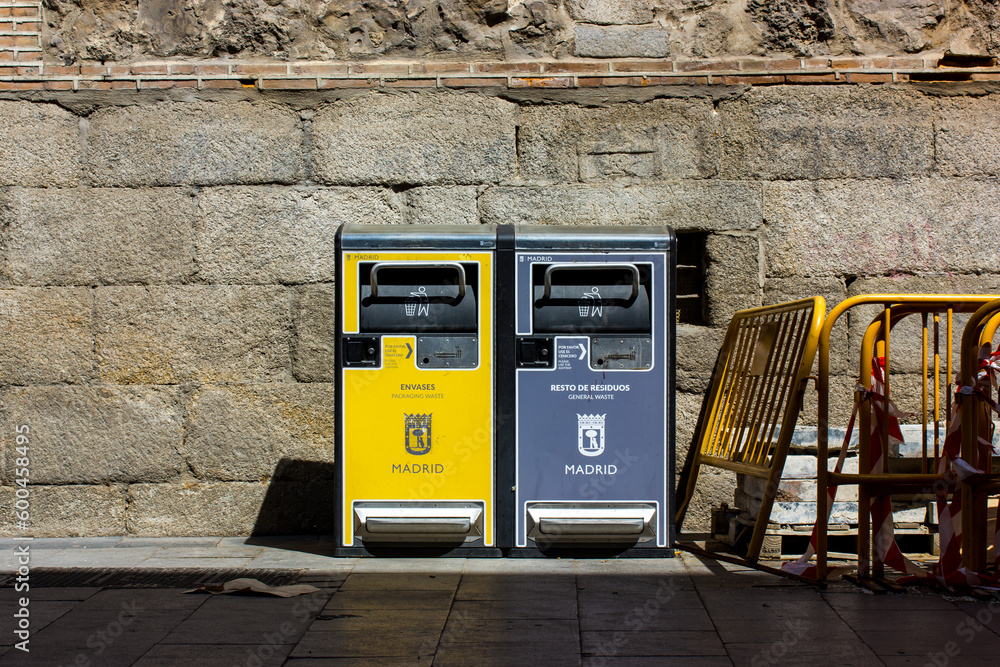 Foto de Madrid, Spain. May 1, 2022 Two gray and yellow trash cans on a