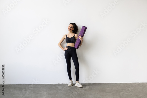 Sports woman holding a fitness mat in her hands on a white background