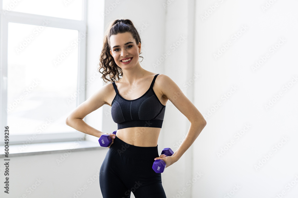 Slim sporty woman doing exercises with small dumbbells at studio