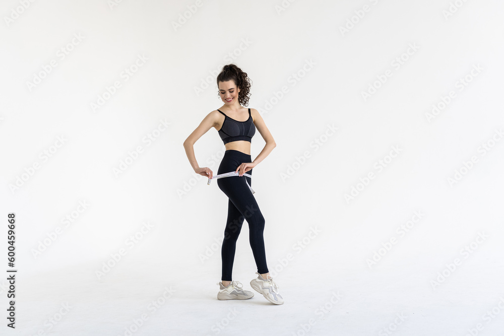 Smiling young woman with beautiful body measuring thigh with measurement type after diet, isolated on white background Smiling young woman with beautiful body measuring thigh with measurement type after diet, isolated on white background
